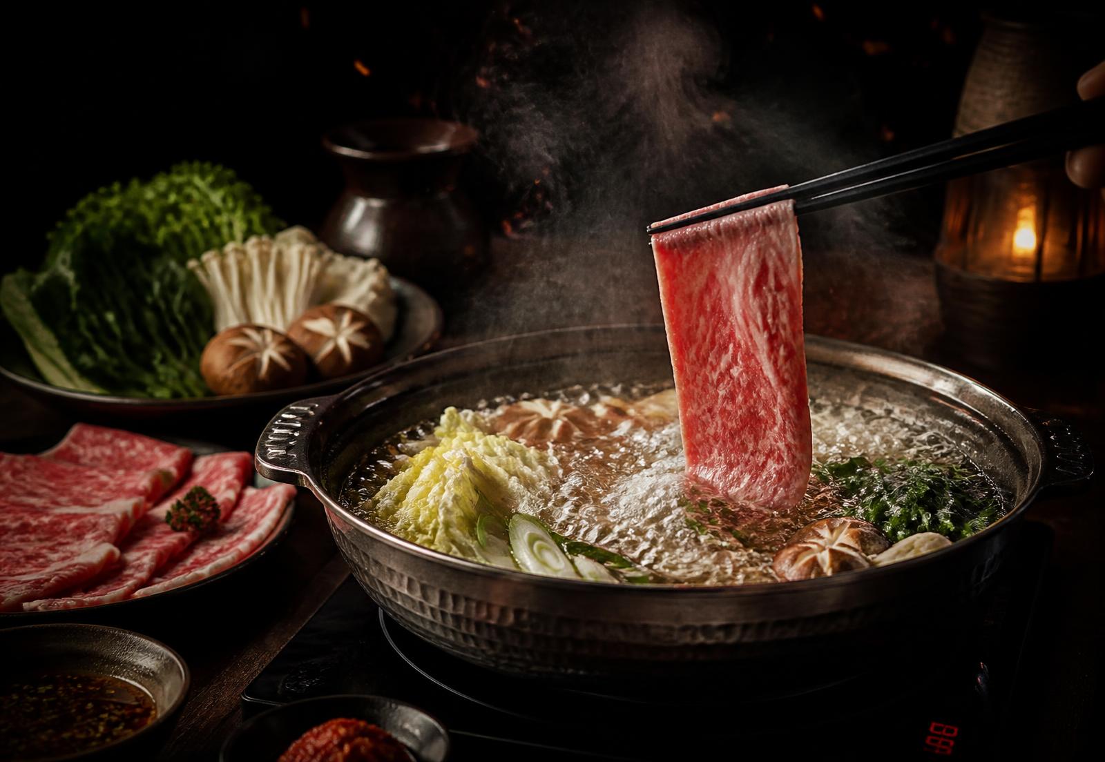 Shabu shabu hot pot with a slice of marbled beef held by chopsticks